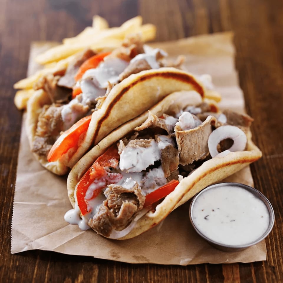 Two gyros with meat, tomatoes, onions, and tzatziki sauce, served with fries and extra sauce.