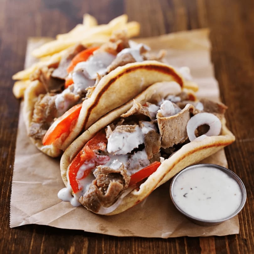 Two gyros with meat, tomatoes, onions, and tzatziki sauce, served with fries and extra sauce.
